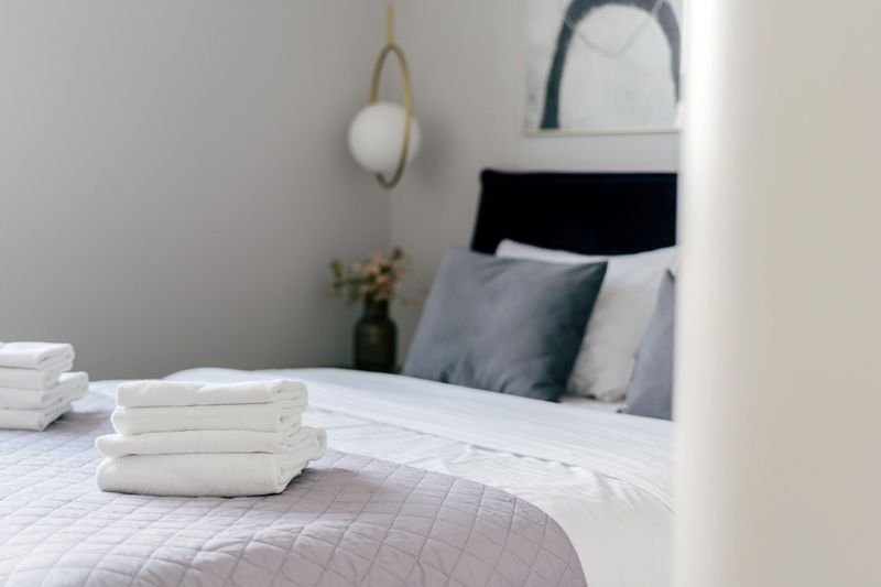 The hotel room features a stylish and neat bedroom with a comfortable bed. Freshly folded linens and decorative pillows create a welcoming environment perfect for relaxation.