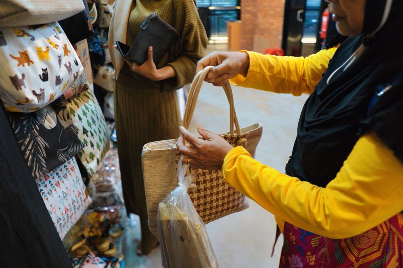 Women inspecting handmade and durable woven bags at a marketplace featuring creative items. Emphasizes craftsmanship, offers diverse bag styles, and represents artistic shopping experiences