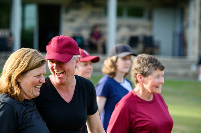 Mixed age range of women and girls practicing cricket on warm summer evening on a grass cricket pitch