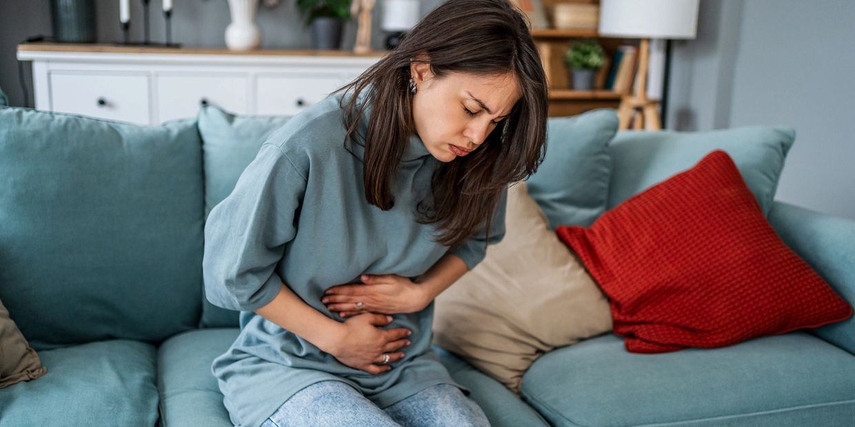 Woman sitting on a couch, clutching her stomach in pain.