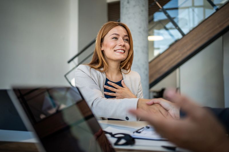Grateful businesswoman shaking hands with her partner, celebrating good news in a modern office, radiating happiness and appreciation for a successful partnership and future opportunities