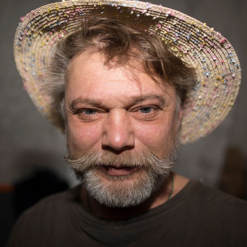 A man with facial hair sporting a straw hat and a wellgroomed beard, emphasizing his defined jawline. He exudes charm and style with his choice of headwear