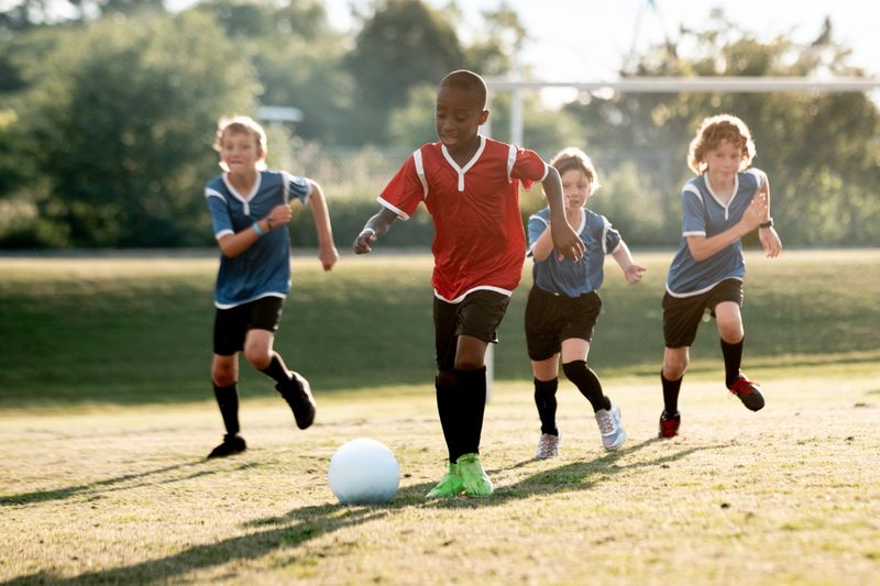 Energetic young boys engage in a lively soccer game on a grassy field under the sun. The action captures teamwork, competition, and sportsmanship while embracing the joy of outdoor childhood activities.