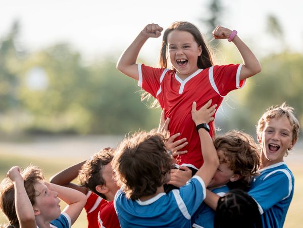 Girl in red jersey lifted by teammates in blue, celebrating victory.