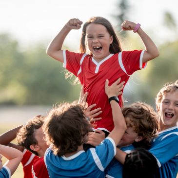 Young girl celebrating victory with teammates in soccer.