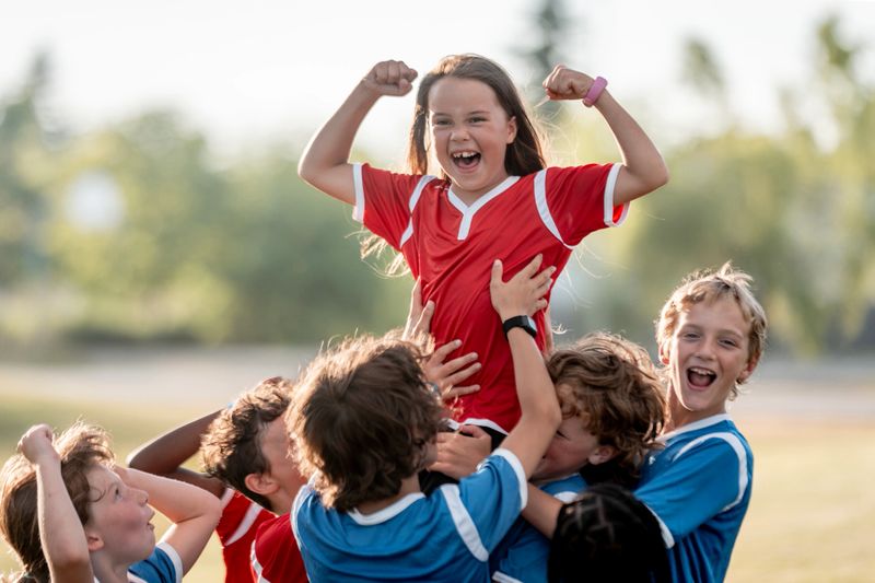 A joyful youth soccer team celebrates their victory as teammates lift a smiling player skyward outdoors, expressing unity and happiness, creating a vibrant and cheerful sports scene embodying team spirit.