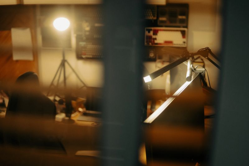 A quiet, intimate look into a cinematic desk setup through window blinds. The soft warm lighting and blurred lines evoke a nostalgic and reflective atmosphere, like a moment paused in time.