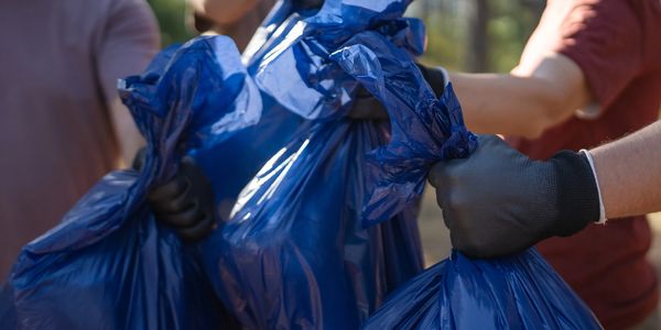 People wearing gloves holding blue garbage bags outdoors.