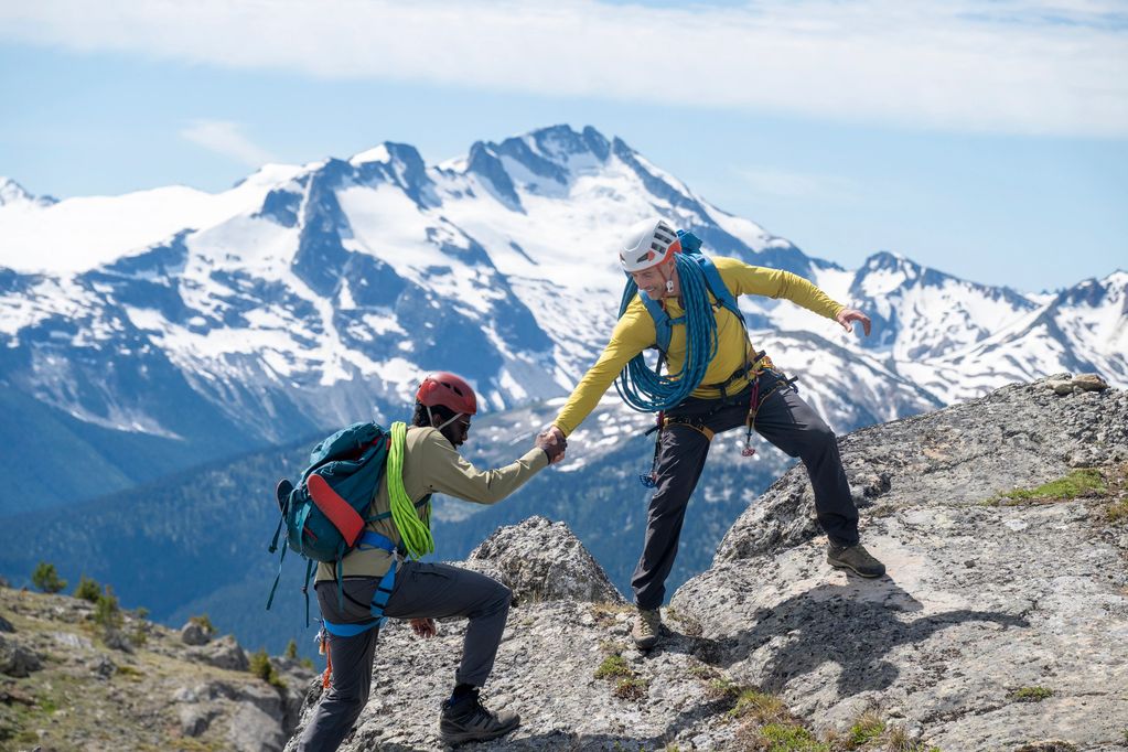 Two climbers help each other on a rocky mountain.