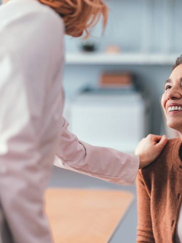 A woman smiling while another person places a hand on her shoulder.