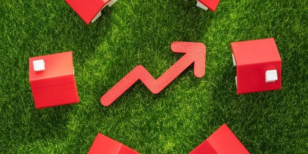 Red arrow among small red houses on green grass, symbolizing growth.