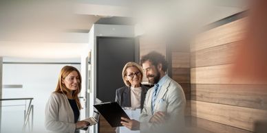 Three colleagues in a modern office discussing work with smiles.