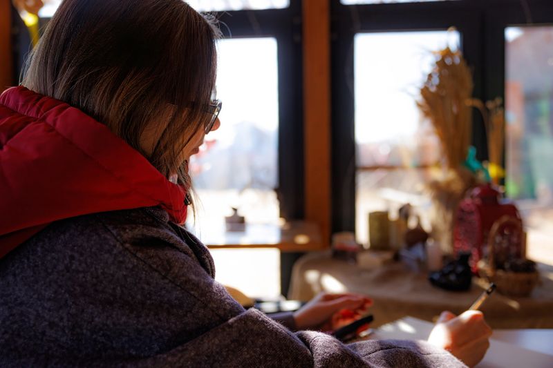 In a cozy setting, a person with glasses writes thoughtfully, illuminated by warm sunlight streaming in.