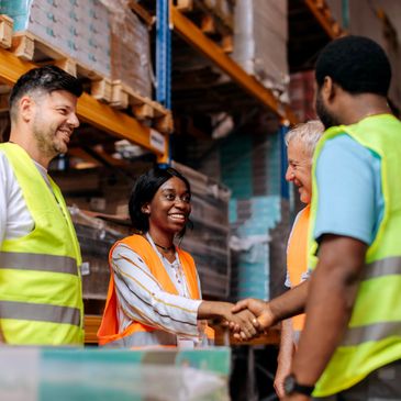 Warehouse workers in safety vests shaking hands and smiling.
