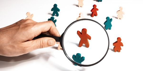 Magnifying glass highlighting a red wooden figure among many colored figures.