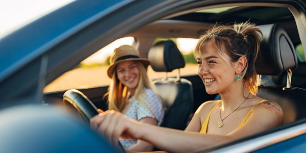 Two women happily sitting in a car during sunset.