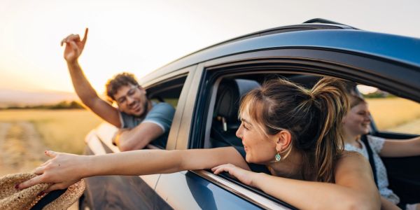 Friends enjoying a road trip, reaching out the car window.