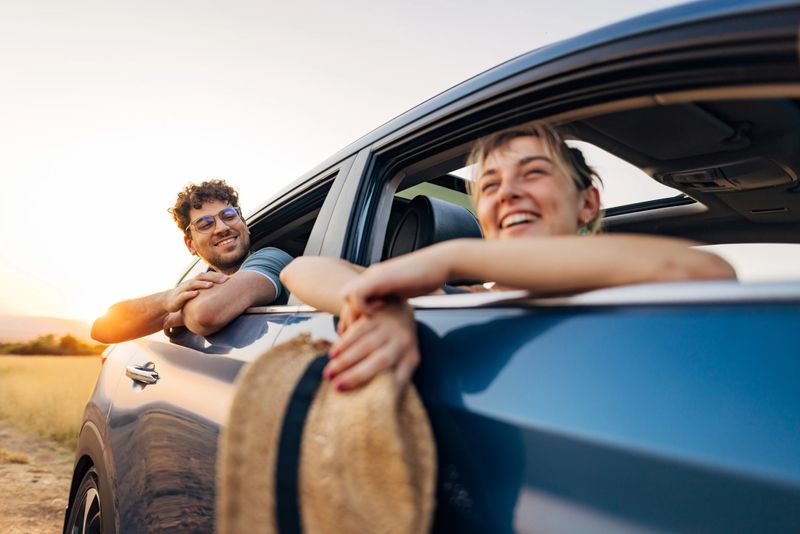 A man and a woman stuck their heads and hands out of the car window and are having crazy fun.