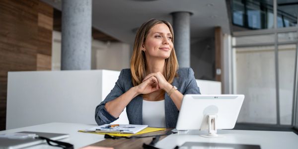 Confident woman sitting at office desk with tablet.