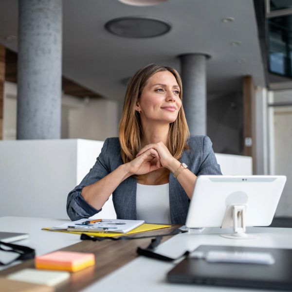 Woman in business attire looking thoughtfully away at workspace.
