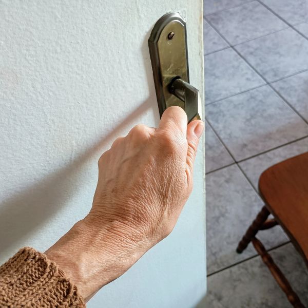 Hand gripping an old brass door handle on a white door.