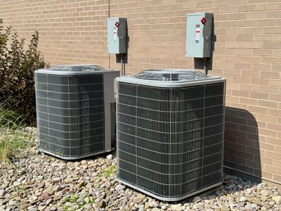 Two outdoor air conditioning units against a brick wall.