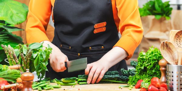 Person chopping fresh green vegetables on a wooden board in a kitchen.