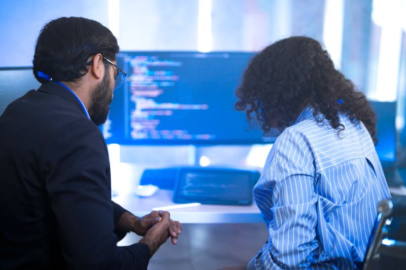 Diverse AI tech team reviewing code for a machine learning algorithm. Indian male and Hispanic female programmers collaborating on artificial intelligence development.