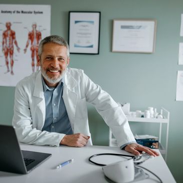 Smiling male doctor sitting at a desk in a medical office.