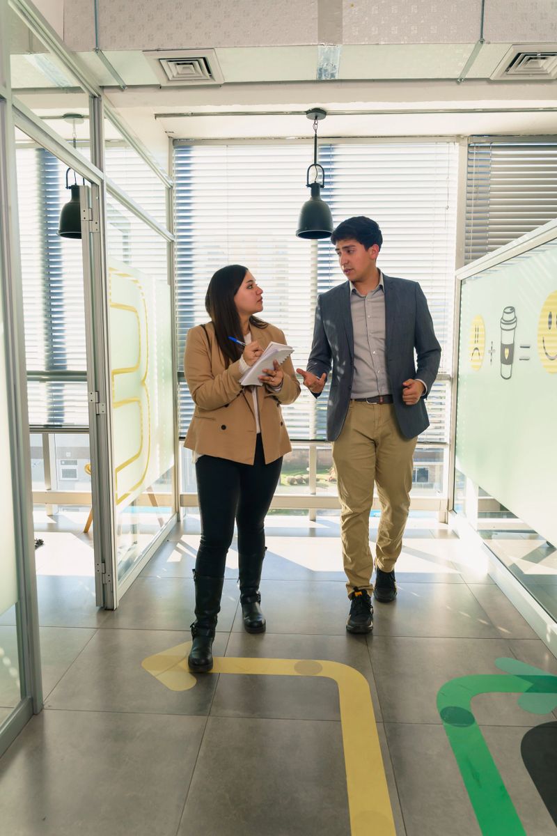 Young latin american professionals walking and talking in office hallway, discussing a project