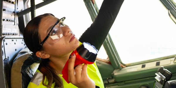 Technician inspects airplane cockpit panel with flashlight.