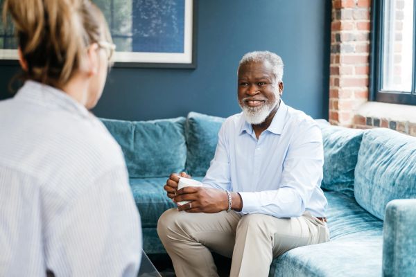Smiling elderly man having a conversation on a blue couch.