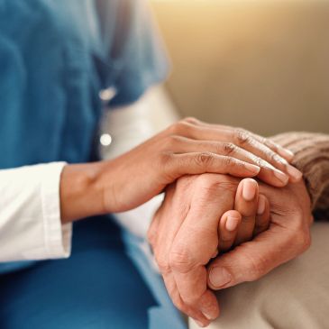 A healthcare professional comforting an elderly patient by holding their hand.