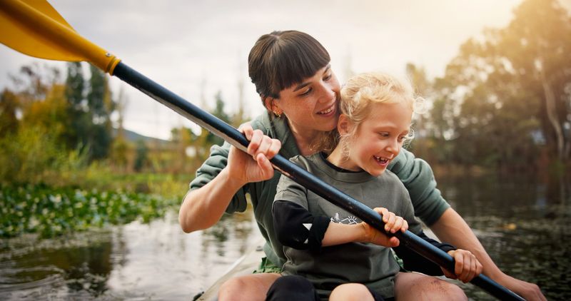 Kayak, mother and child with support in lake, water activity and adventure for bonding together. River, mom and girl with paddle to learn canoeing, travel holiday and rowing outdoor as family in boat