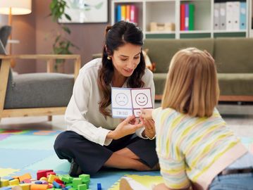 Woman showing a child an emotions chart.