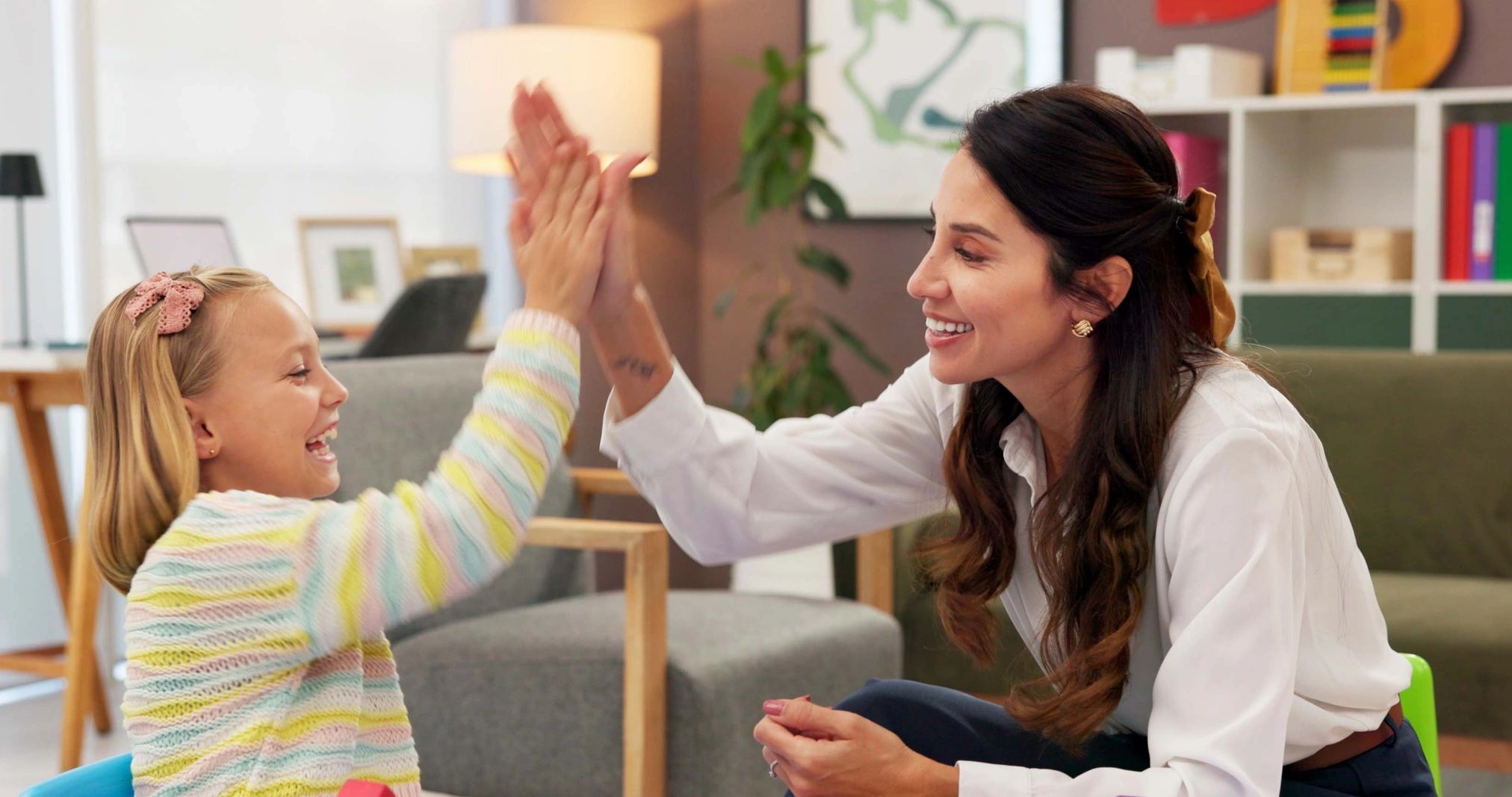 A woman and a girl happily high-five indoors.