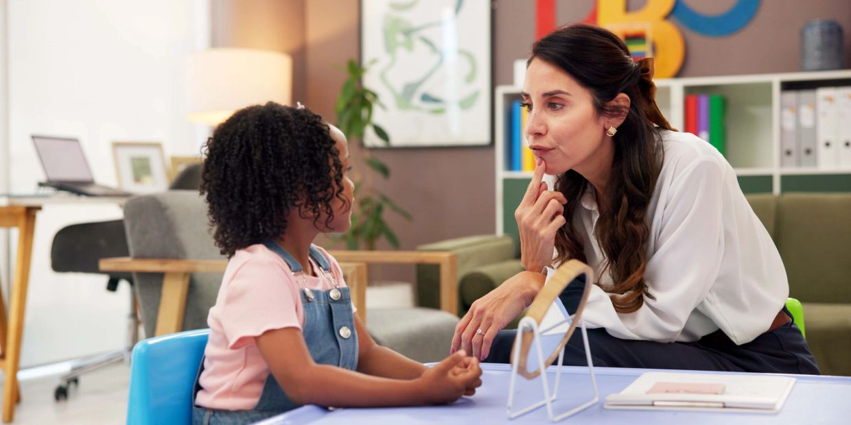Woman attentively listening to a young girl indoors.