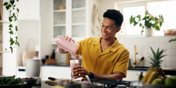 Man pouring a pink smoothie in a kitchen.