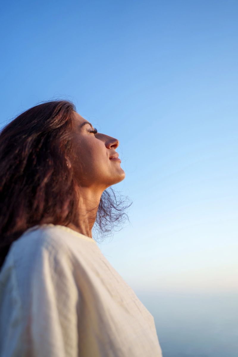 Side view portrait of a young woman breathing deeply fresh air with closed eyes against a blue sky