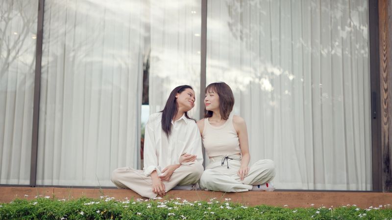 LGBTQ couple spend their weekend getaway at a cozy resort nestled in the mountains, sitting along flower paths and enjoying morning on the hotel balcony. They smile, embrace, and cherish simple joys as part of their everyday life full of love and peace.