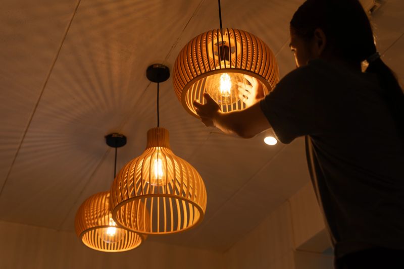 Close up of a person adjusting glowing wooden pendant lamp on ceiling in warm cozy room, modern stylish home interior lighting, creative use of energy for comfort, ambiance, and elegant decoration