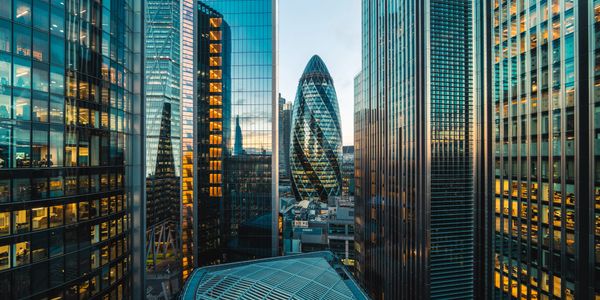 Cityscape featuring modern glass skyscrapers and the iconic Gherkin building at sunset.