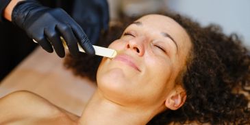 Woman receiving a facial waxing treatment with eyes closed.