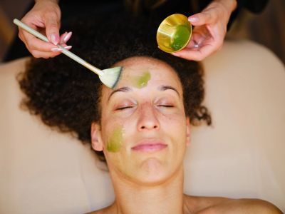 Woman getting a green facial mask applied.