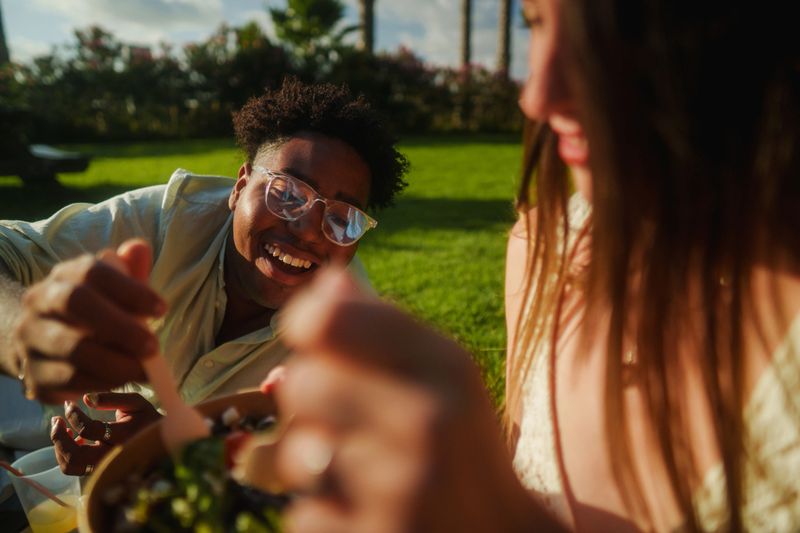Cheerful friends sharing a healthy meal outdoors, enjoying the summer vibes during a picnic in the park