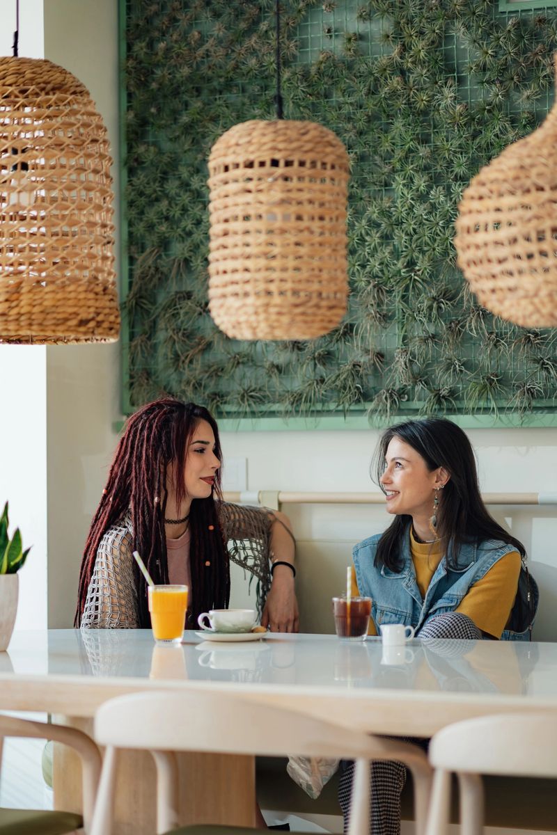 Two female friends are catching up over drinks at a stylish cafe, enjoying each other's company in a vibrant setting