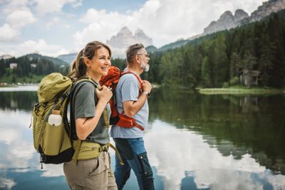 A couple hiking near a serene lake with mountains in the background.