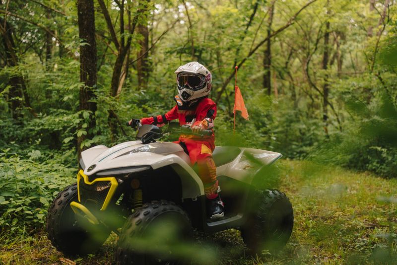 A brave, little girl rides her quad bike across a trail surrounded by trees and nature. Outdoor fun and freedom on four wheels