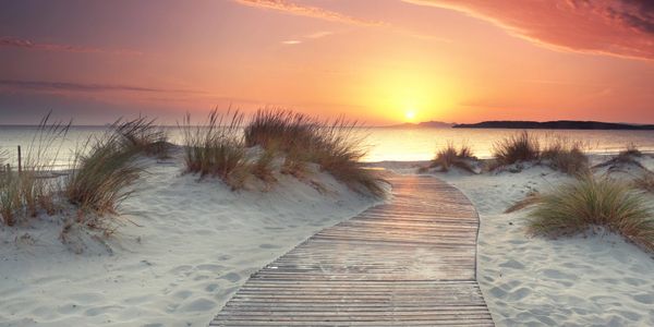 Wooden pathway leading to a serene beach sunset over calm waters.