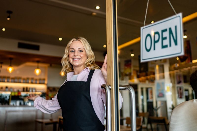 Portrait of mid adult waitress welcoming customers to coffee shop